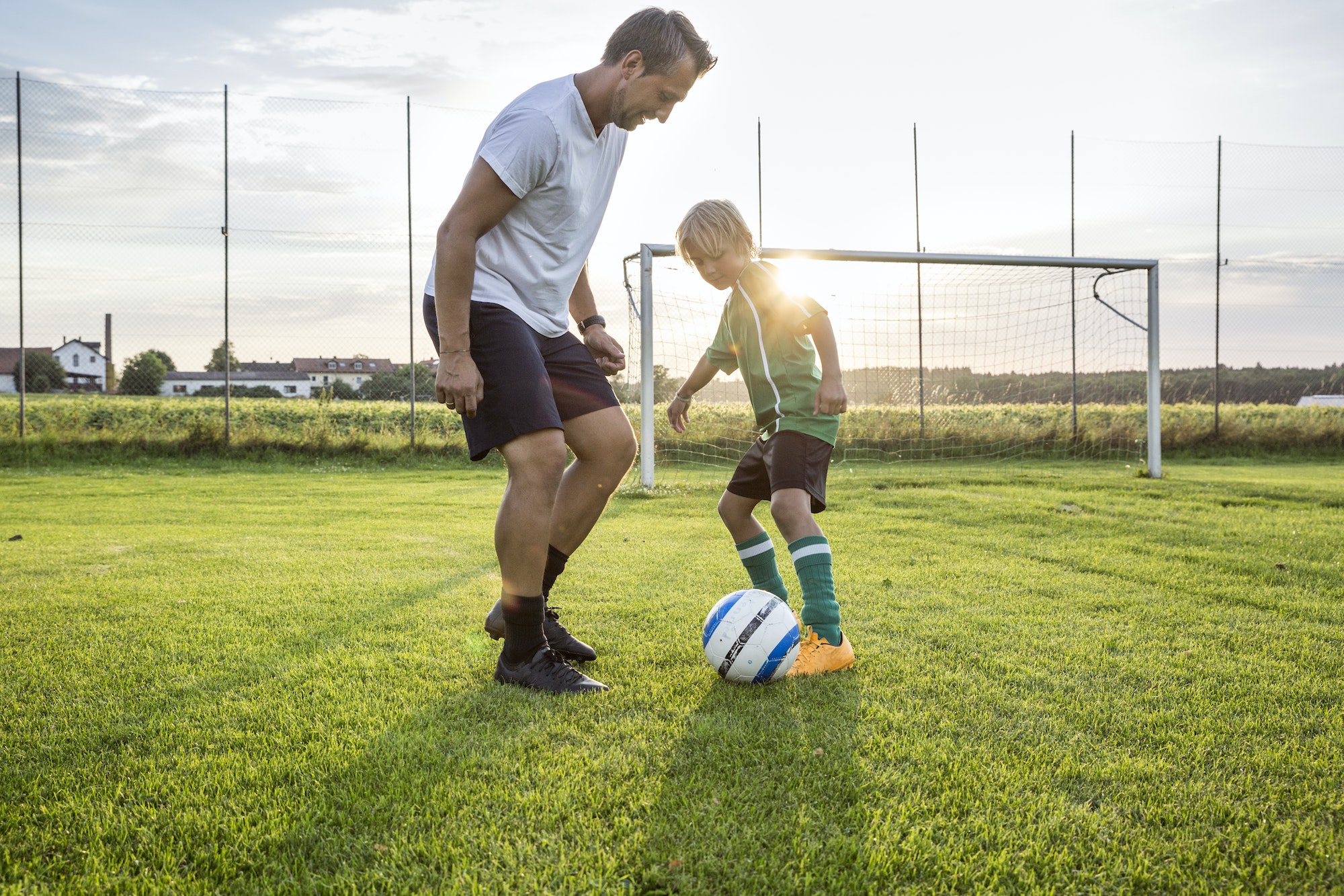 Coach and young football player on football ground at sunset